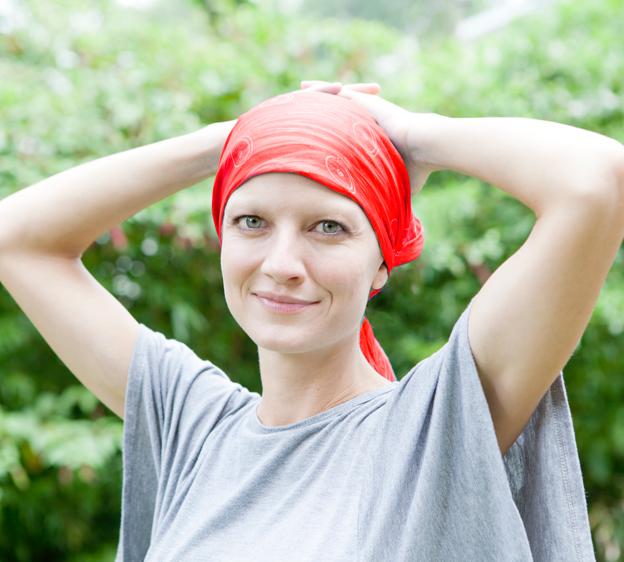 A cancer survivor wearing a red bandana and gray shirt is outside enjoying the weather